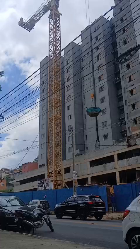 Grua de torre içando carga ao lado de um edifício em construção